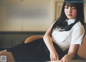 A woman in a white shirt and black tie sitting on a red couch.