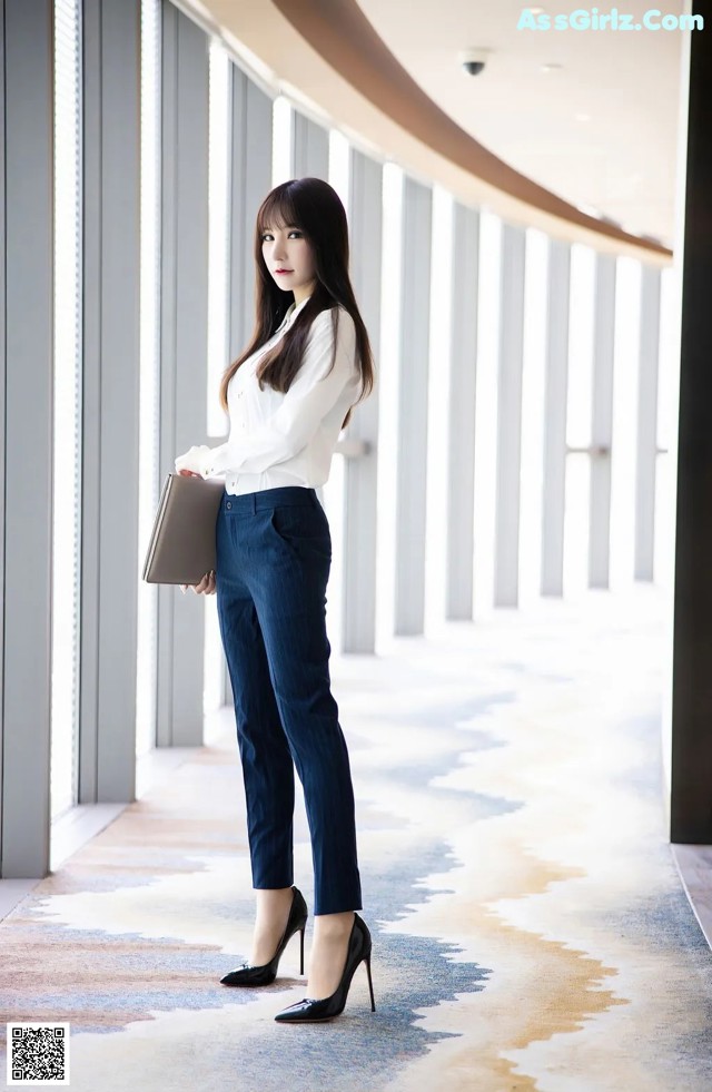 A woman in a white shirt and blue pants holding a laptop.