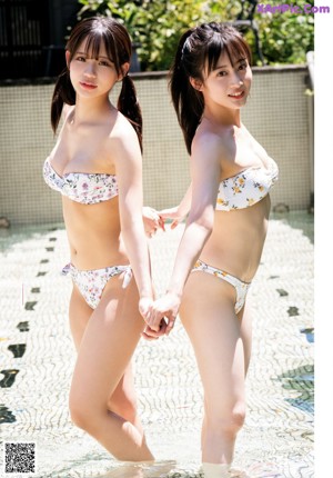 Two young women in bikinis sitting on a wooden bench.