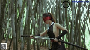 A woman in a black dress holding a sword in a forest.