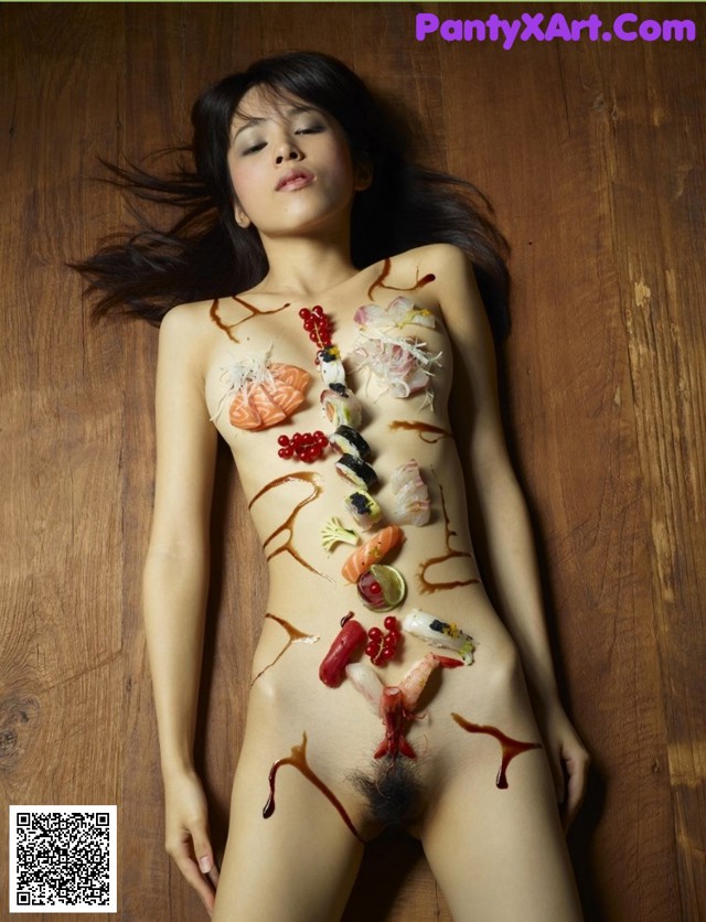 A naked woman laying on a wooden floor covered in sushi.