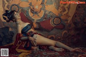 A woman in a red and gold outfit sitting on a rug.